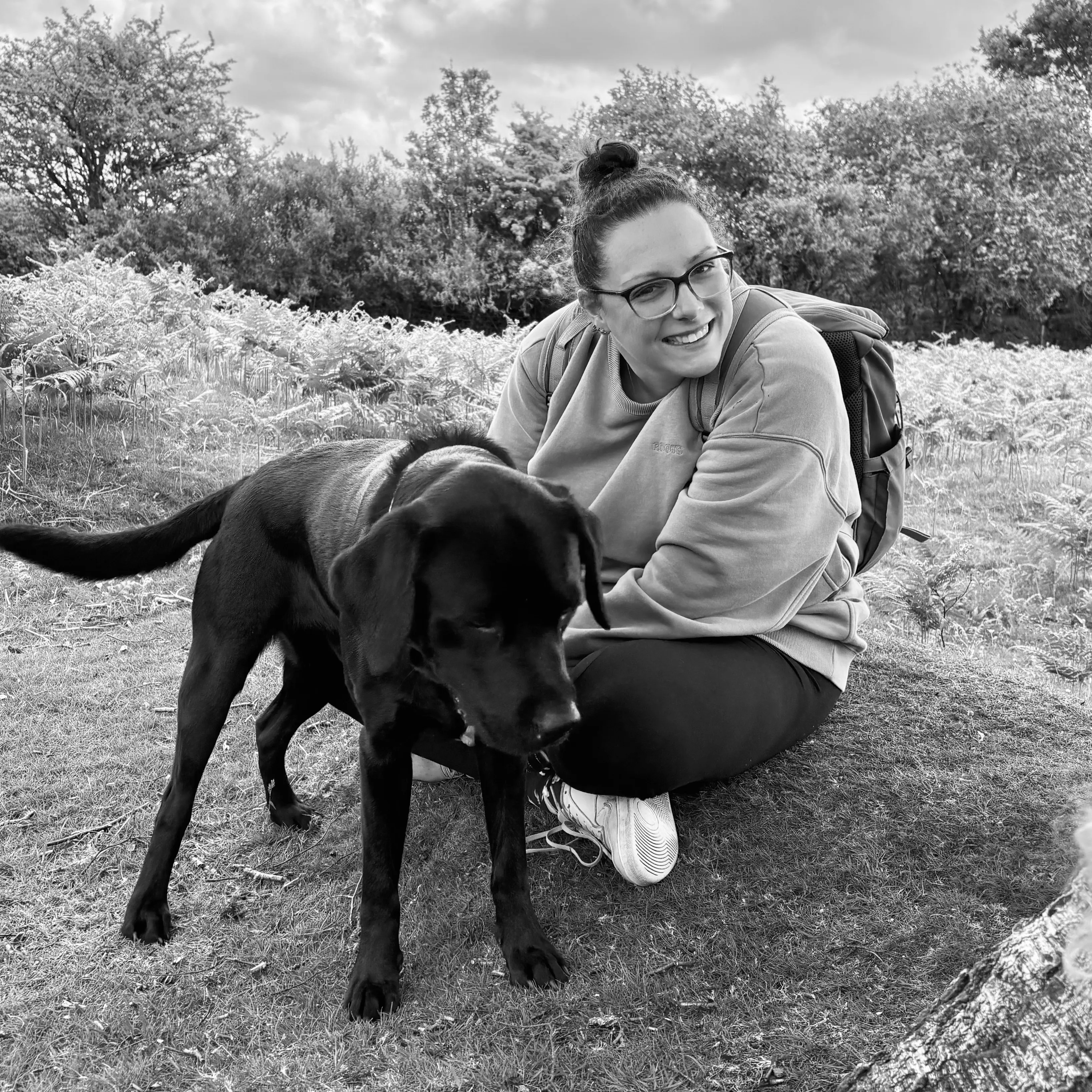 Kirsty sitting on the grass with a black Labrador